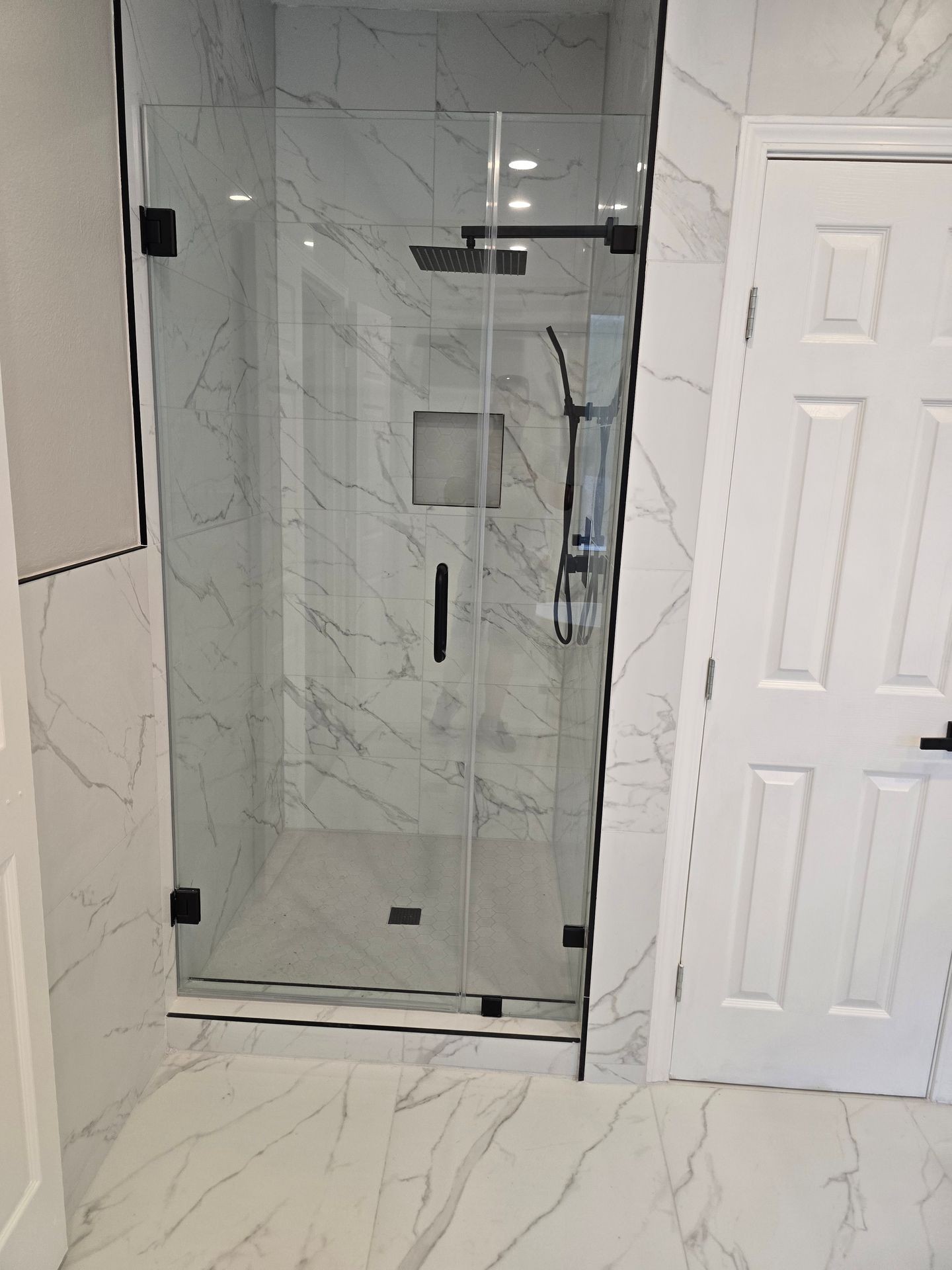 Modern bathroom with glass shower door and marble tile walls.