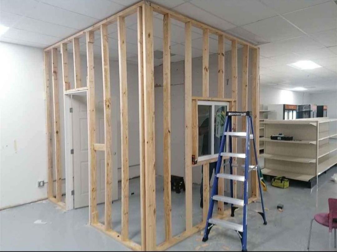 Partially constructed interior room with exposed wooden framing and a ladder standing nearby in a store.